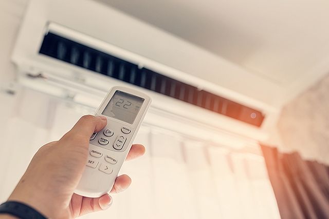 Hand mit Fernbedienung richtet sich auf eine Klimaanlage an der Wand