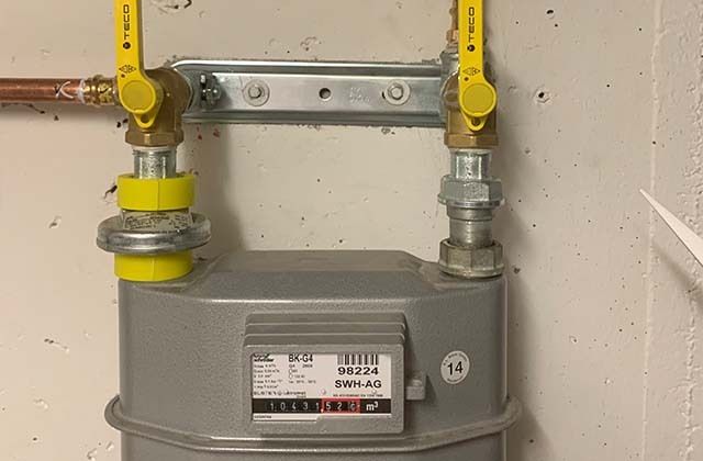 Gaszähler mit gelben Absperrhähnen und Leitungen an einer Wand montiert