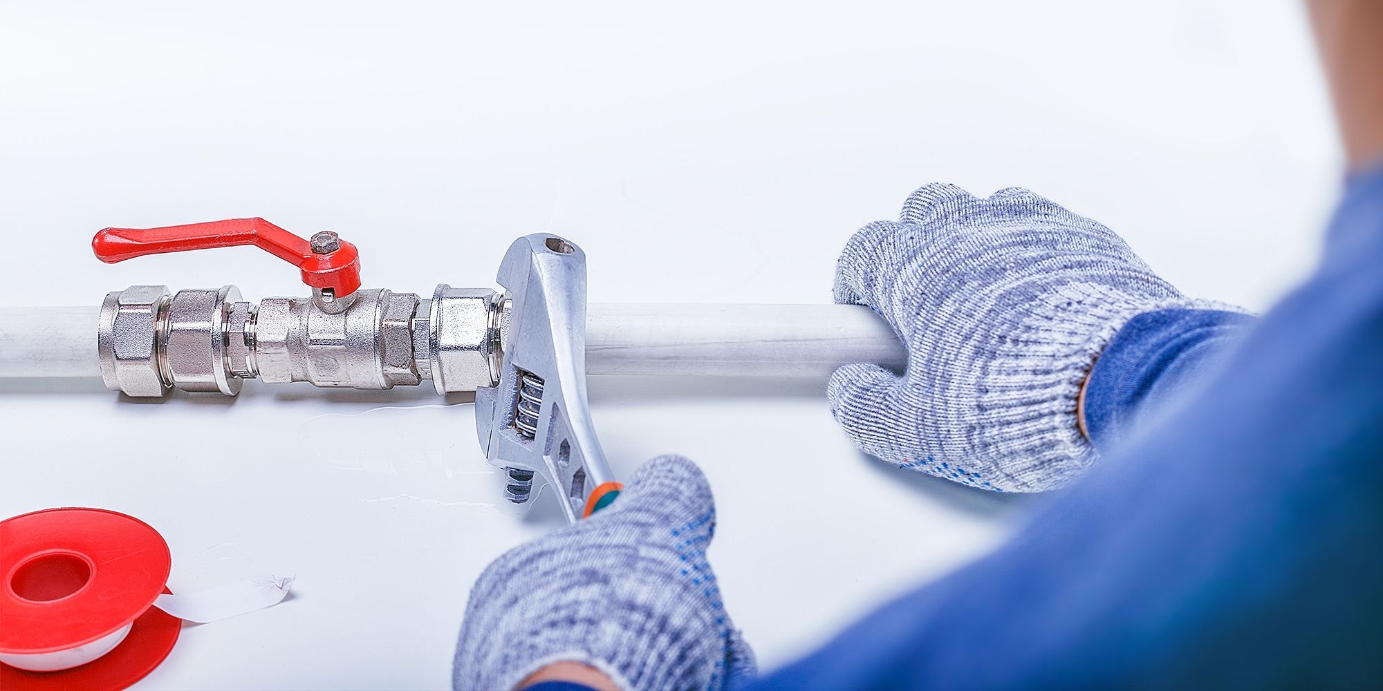 Person mit blauen Arbeitshandschuhen arbeitet mit einem Schraubenschlüssel an einem Metallventil